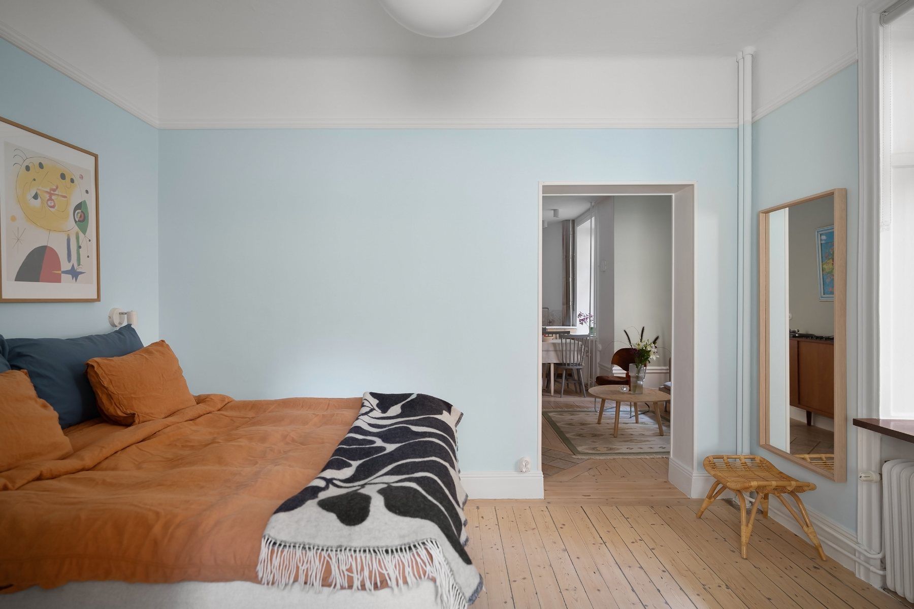Chambre aux murs bleu ciel, linge de lit orangé et parquet clair