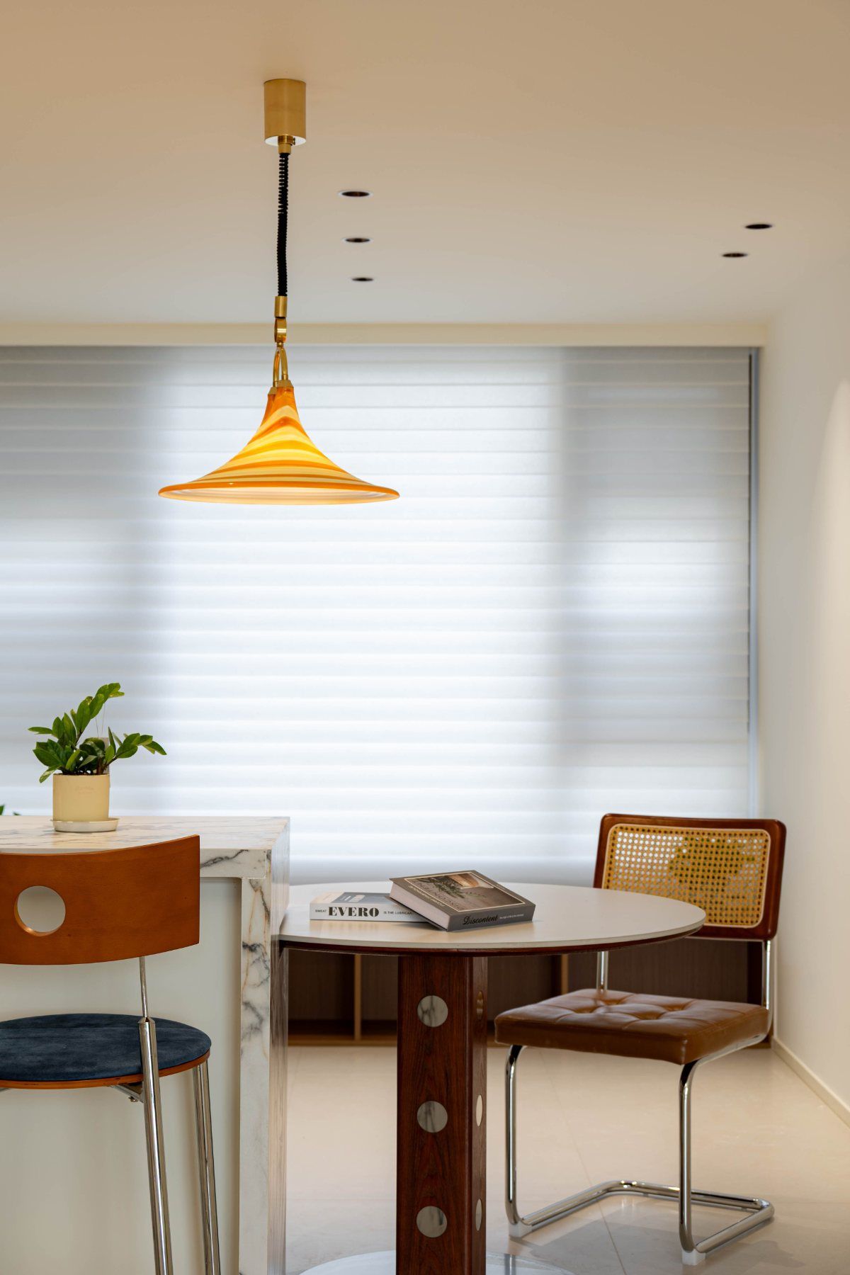Suspension en verre rayé orange au-dessus d'une table ronde et de chaises en cuir cognac