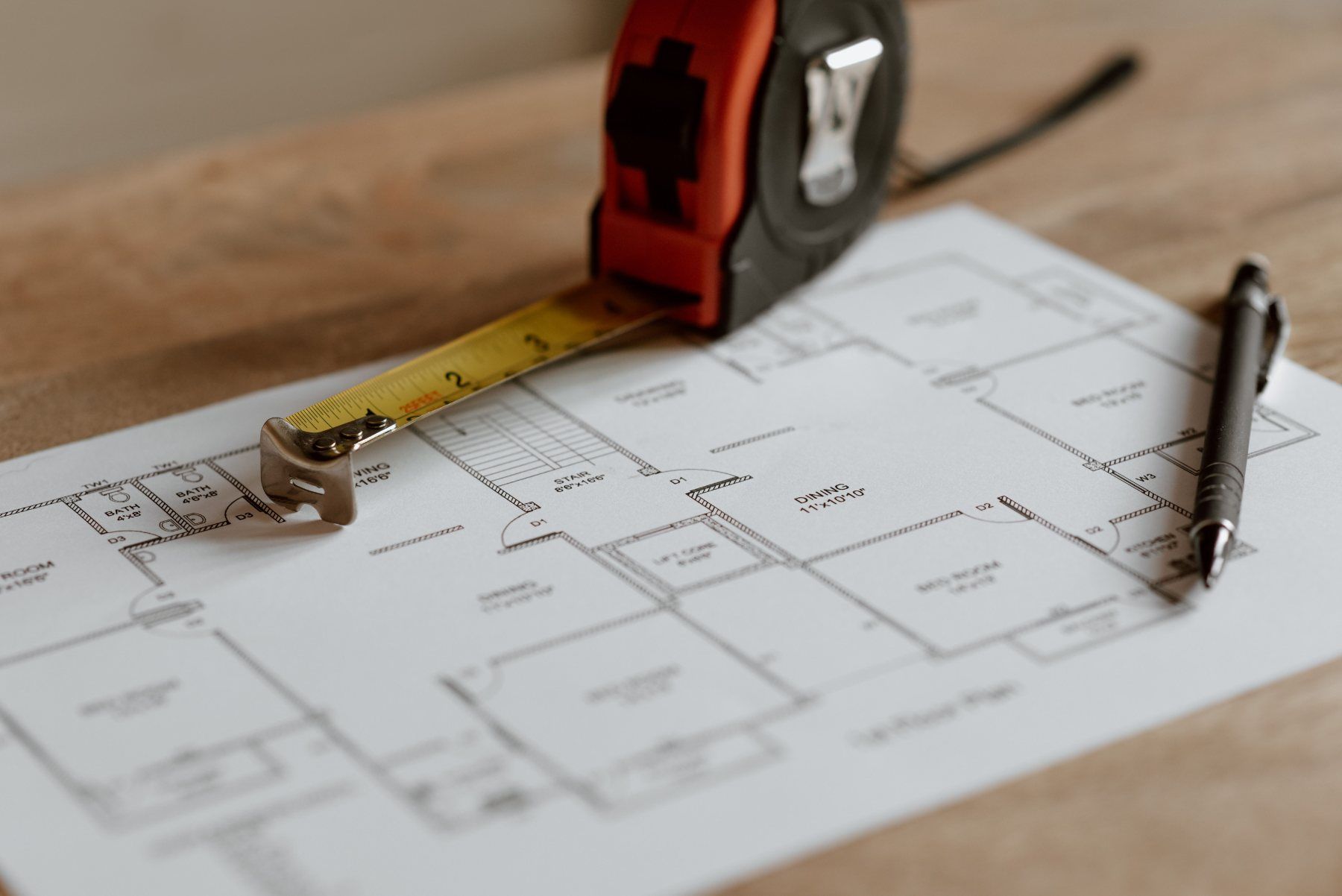 Plan d'appartement imprimé, mètre ruban et stylo posés sur une table
