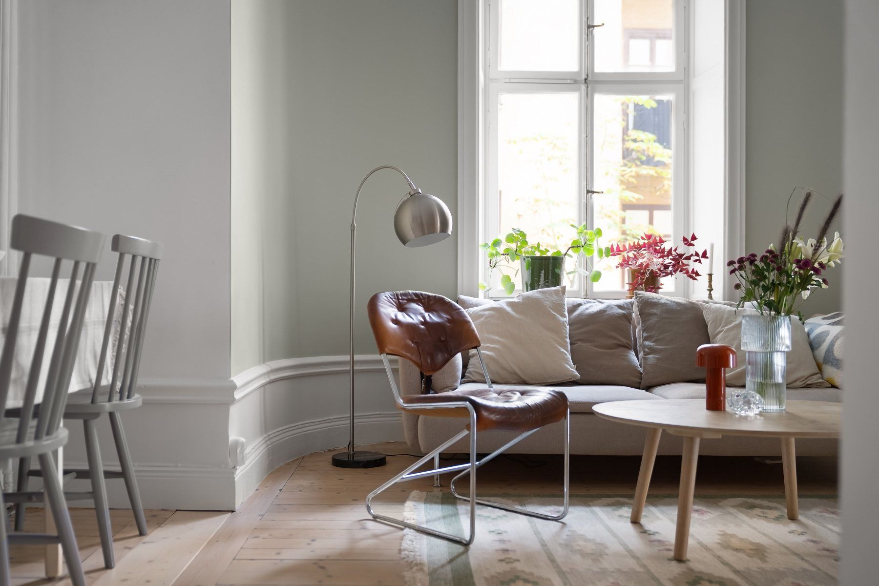 Séjour baigné de lumière naturelle : grande fenêtre, plantes, canapé en lin et fauteuil en cuir
